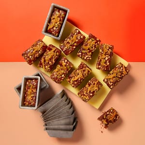 A full tray of vegan Sticky Ginger and Lemon Mini Loaf cakes by Cake Club on a yellow board with an orange and peach contrasting background.