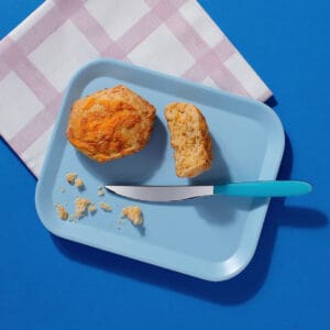 The Big Cheese cheese scone broken open on pastel plate beside knife and napkin.