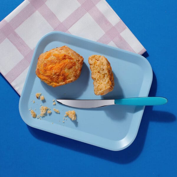 The Big Cheese cheese scone broken open on pastel plate beside knife and napkin.