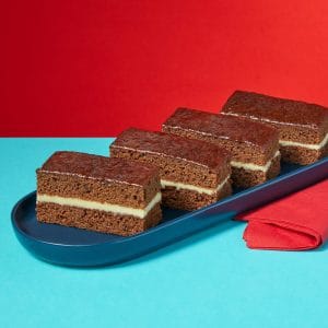 Rum and Ginger Traycake slices on a dark blue plate against a red background.