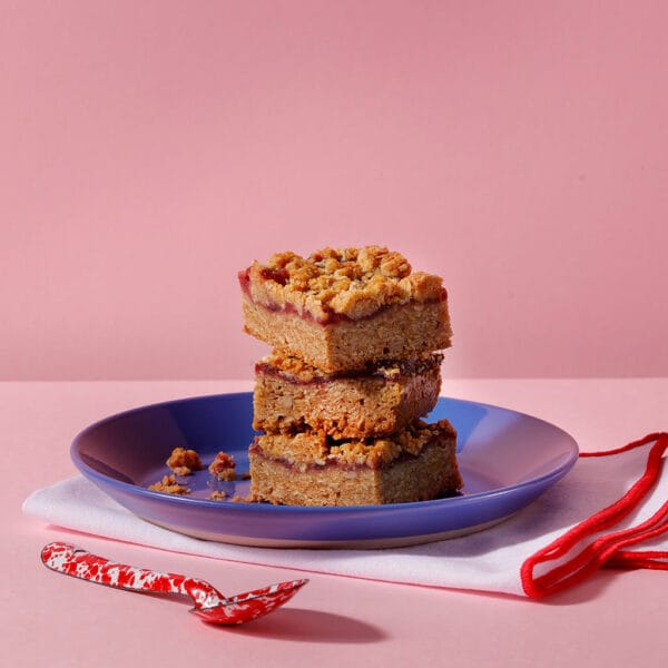 Vegan Berry Crumble stacked oat flapjack bars with berry jam filling on blue plate – Cake Club vegan bake.