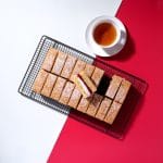 Overhead view of 18 slices of victoria sponge traycake on a red and white background.