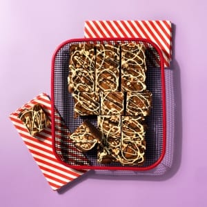 A whole tray of Salted Caramel and Comb Brownie on a cooling rack with red and white striped napkin on a light purple background.