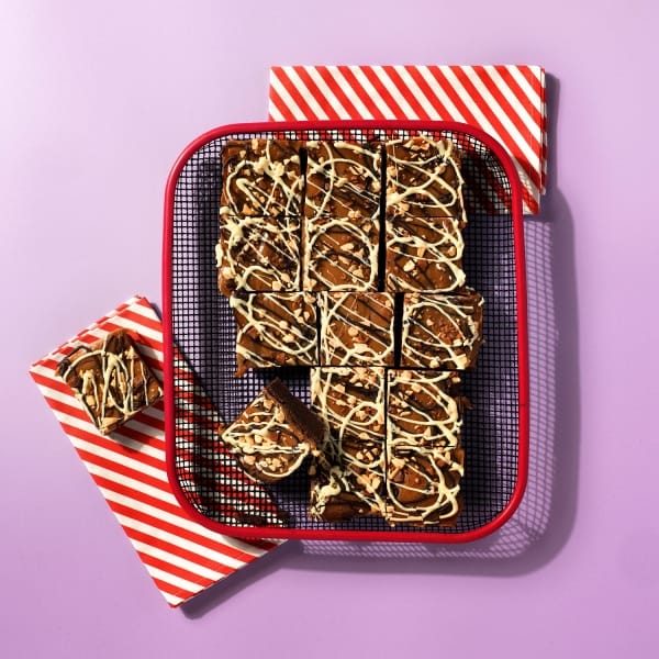 A whole tray of Salted Caramel and Comb Brownie on a cooling rack with red and white striped napkin on a light purple background.
