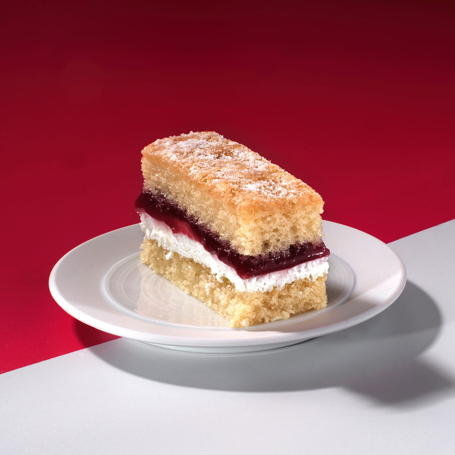 Close-up of Victoria Sponge Traycake slice with jam and cream layers on white surface.