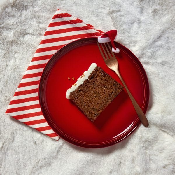 A single slice of rum and raisin Christmas loaf cake on a red plate with a striped napkin and spoon.