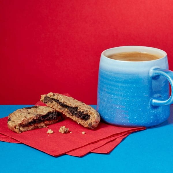 Loaded Chocolate Chip Cookie broken open on a blue plate against a red background.