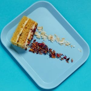 Passionfruit and Coconut Traycake sliced on a blue tray with scattered coconut and petals.