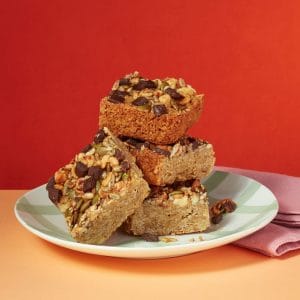 Roasted Hazelnut Flapjack pieces stacked on a plate against a red background.